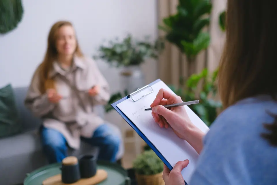 Clinician writing notes on a clipboard while a client talks during a session